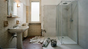 Bagno a metà ristrutturazione, a sinistra le vecchie piastrelle beige, a destra il nuovo rivestimento con box doccia in cristallo e piatto bianco